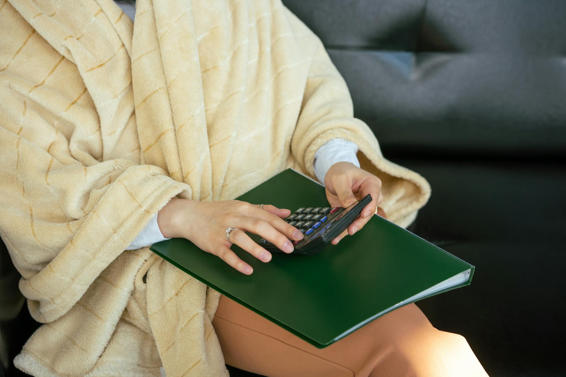 Dłonie w szlafroku liczące koszty ocieplenia domu na kalkulatorze