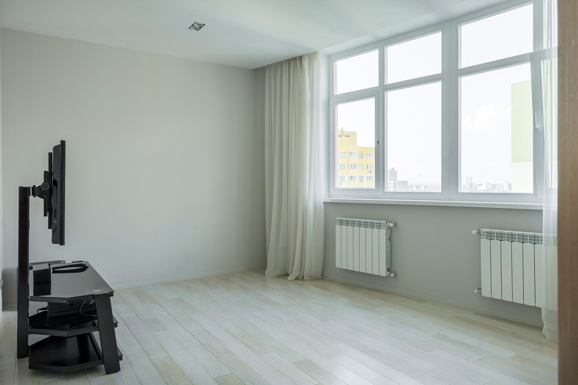 Jasny minimalistyczny salon w bloku z dużymi oknami i drewnianą podłogą